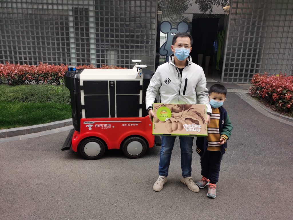 Mr. Hu and his son holding Zespri kiwifruit in front of a JD autonomous delivery robot