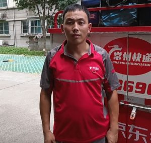 Ma Hao dressed in his signature red JD Courier uniform standing in front of his delivery tricycle